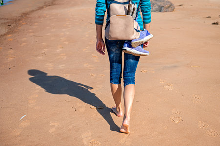 woman with backpack walking barefoot on beach during a sunny day, rear view, close-upの写真素材