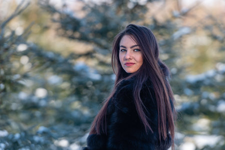 cheerful young woman in a warm fur coat enjoying a winter day in the snowy forestの写真素材