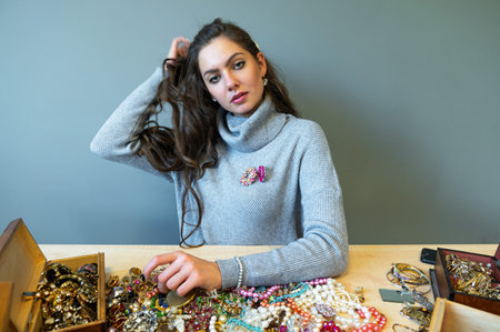 slim brunette sitting at the table with lots of jewelry, choosing and trying different jewelry