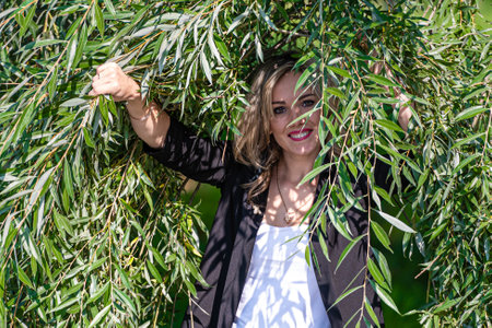 Portrait of young beautiful woman with natural makeup looking through green willow branchesの写真素材