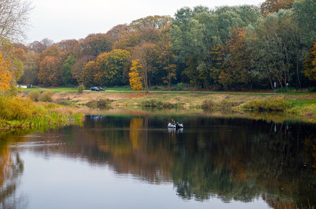 fisherman in a rubber boat on the river and colorful autumn trees on the shore on a cloudy dayの写真素材