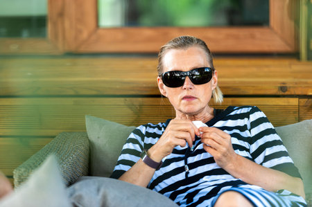 emotional blond middle - aged woman relaxing on the couch in the shade of a tree on a sunny dayの写真素材
