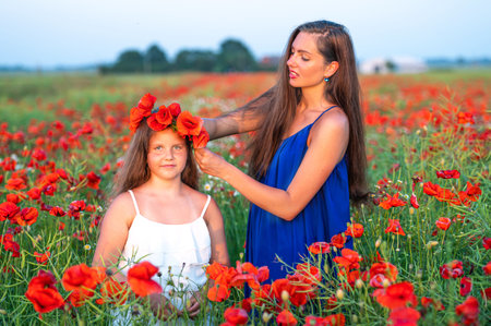 beautiful young woman with child girl in poppy field, happy family having fun in nature, summer timeの写真素材
