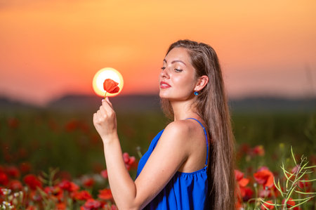 pretty young woman playing with sun ball while standing in poppy field in warm sunset lightの写真素材