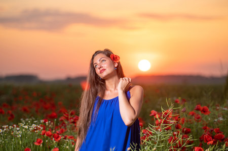 pretty young woman playing with sun ball while standing in poppy field in warm sunset lightの写真素材