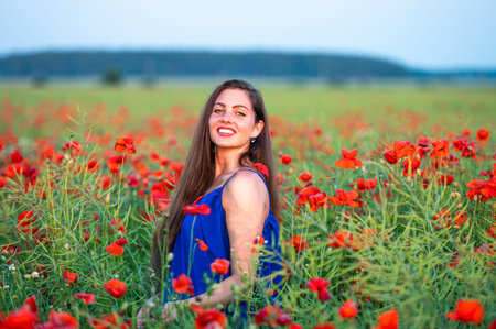elegant young woman with long hair playing with petals in poppy field in evening sunlightの写真素材