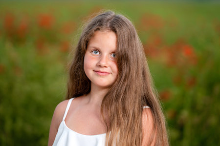 portrait of a little girl against the background of a field of poppies in the evening sunlightの写真素材