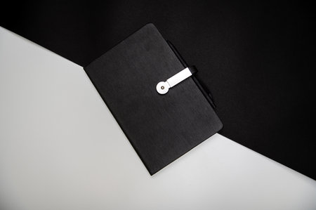 black planner or notebook with pen on two-color black and white background, mockup, copy spaceの写真素材