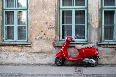 A red vintage scooter on a pedestrian sidewalk in front of an old stone houseの写真素材