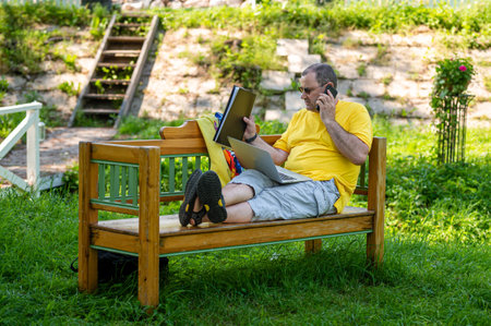 middle aged man with laptop and smartphone working outside in garden, green home office conceptの写真素材