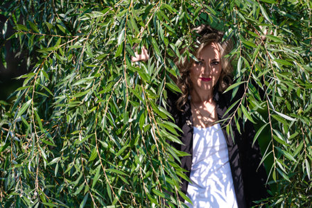 Portrait of young beautiful woman with natural makeup looking through green willow branchesの写真素材