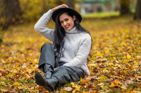 Beautiful young brunette woman in a white sweater and black hat in autumn parkの写真素材