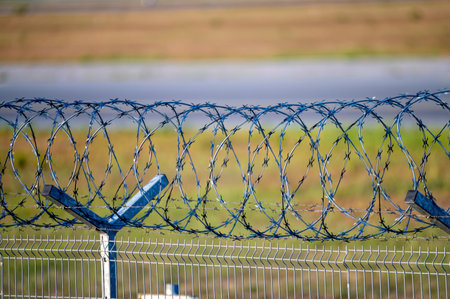 Barbed wire fence on a background of green grass and road. Shallow depth of fieldの写真素材