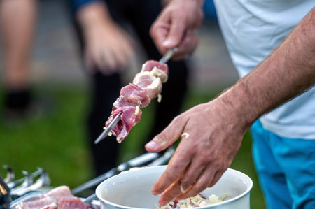 Man cooking meat on barbecue skewer outdoors. Closeup of male hands preparing barbecue meat.の写真素材