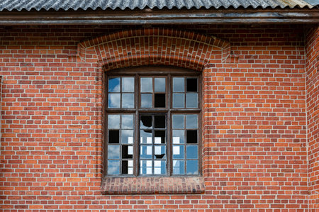 An old window with broken glass panes in a red brick wall. Close-up