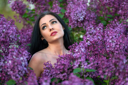 A woman with long black hair poses among purple lilac blossoms. Shallow depth of feldの写真素材