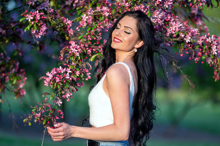 A woman with long black hair stands near a flowering tree. Shallow depth of feldの写真素材