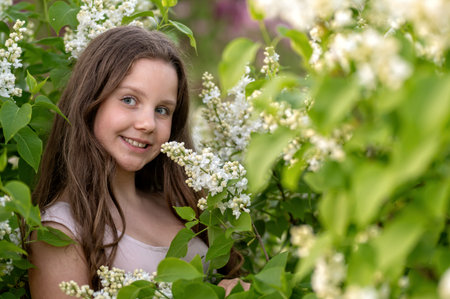 A young girl stands in a blooming lilac bush. Background with selective focus and copy space