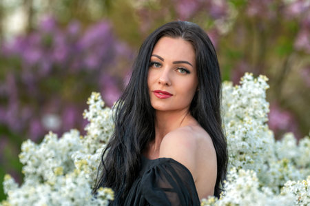A woman with long black hair poses in a garden with white flowers. Shallow depth of feld
