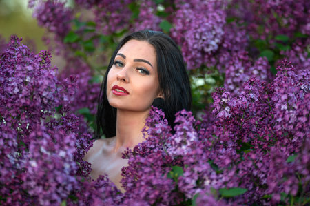 A woman with long black hair poses among purple lilac blossoms. Shallow depth of feldの写真素材