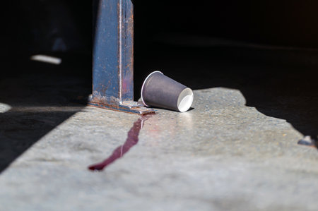 A paper cup lies on the ground, with liquid spilling onto the concrete.