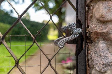 The detailed gate handle highlights the entry to a vibrant garden filled with greenery.の写真素材