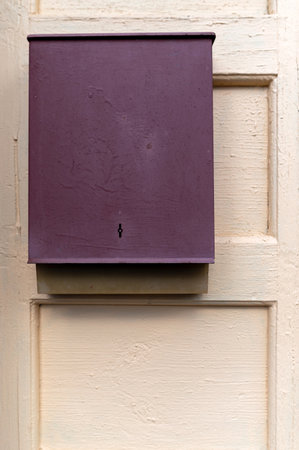 A purple mailbox is attached to a light-colored wooden door, reflecting morning sunlight.