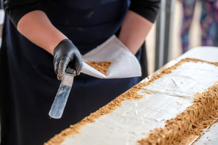 A baker wearing black gloves spreads crumbs around the edges of a white cake. Shallow depth of feldの写真素材