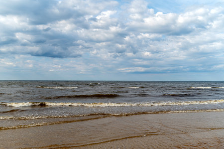 Gentle waves move towards the beach while clouds fill the evening sky.の写真素材