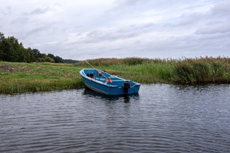 A blue fishing boat is anchored peacefully in a tranquil waterway, framed by lush greenery.の写真素材