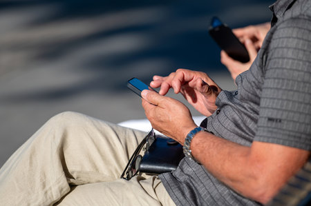 Individual engaged with a smartphone outdoors, enjoying a sunny day with another person.の写真素材
