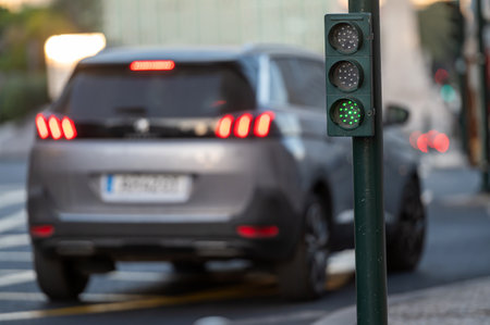 A gray vehicle drives towards a green traffic light in a busy city street.の写真素材