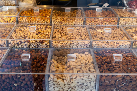 Various types of nuts are arranged neatly in transparent bins at a marketplace.
