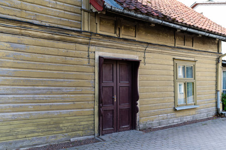A wooden house showcasing a worn facade, featuring a brown door and a green window.の写真素材
