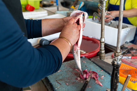 A vendor skillfully cleans fish on a work surface in a busy market setting.の写真素材