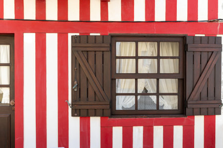 A vibrant striped house features a window with wooden shutters and lace curtains.の写真素材