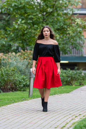A woman strolls down a pathway wearing a stylish outfit amidst autumn foliage.の写真素材