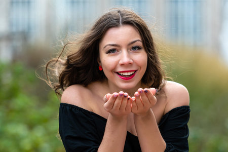 A woman blows kisses while surrounded by greenery and city buildings.の写真素材