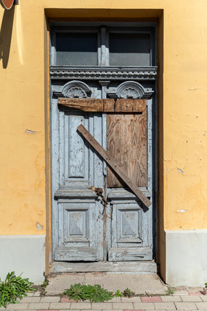 An old blue door with wood planks crossing it stands on a bright yellow wall.の写真素材