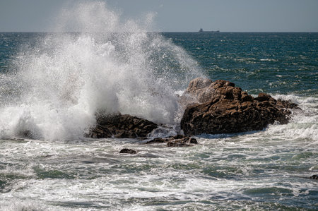 Waves crashing against rocky coast under bright sunlight by the open seaの写真素材