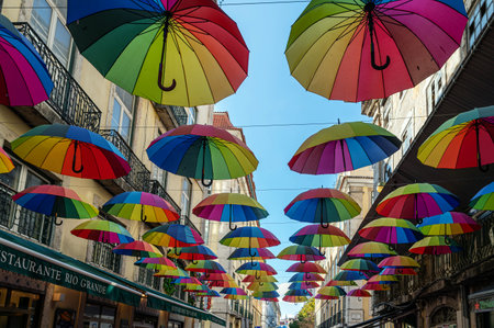 Brightly colored umbrellas are suspended above a lively street under a clear blue sky.の写真素材