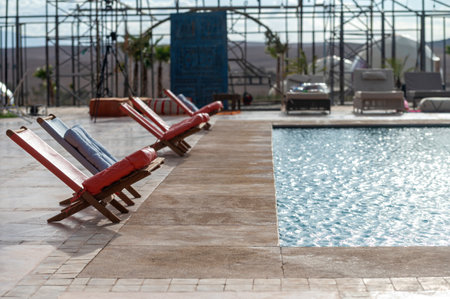 Chairs surround a tranquil pool against the expansive backdrop of the Agafay Desert.の写真素材
