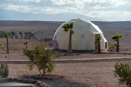 Agafay Desert, Morocco - February 16, 2025: A geodesic dome stands amidst palm trees in the vast Moroccan desert at Agafay.の写真素材
