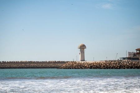 Lighthouse stands on the shore while waves gently roll in, capturing Moroccan coastal beauty.の写真素材
