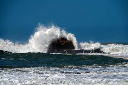 Waves crashing against rocky shore in Essaouira, Morocco during clear blue skyの写真素材