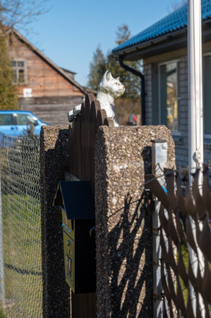Decorative cat atop wooden fence near charming house and mailbox in serene countryside.の写真素材