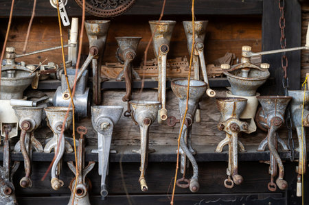 Various antique food grinders are neatly arranged on a weathered wooden shelf in a workshop.