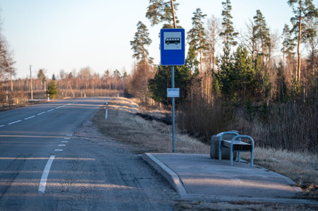 A bus stop is situated beside a tranquil road with trees in the background on a sunny day.の写真素材