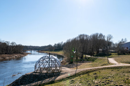 A modern geodesic dome near a calm river offers a serene spot for visitors to enjoy nature.