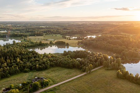 Sunset casts warm light over peaceful lakes and forests, creating a serene landscape view.の写真素材